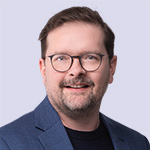 Smiling man with beard and glasses in blue jacket.