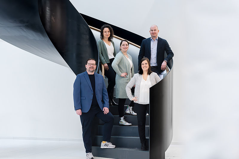 Five professionals posing on modern spiral staircase.