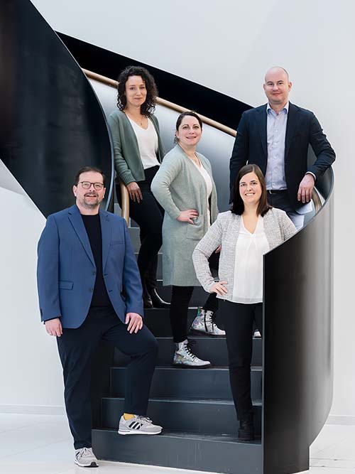 Five professionals posing on modern spiral staircase.